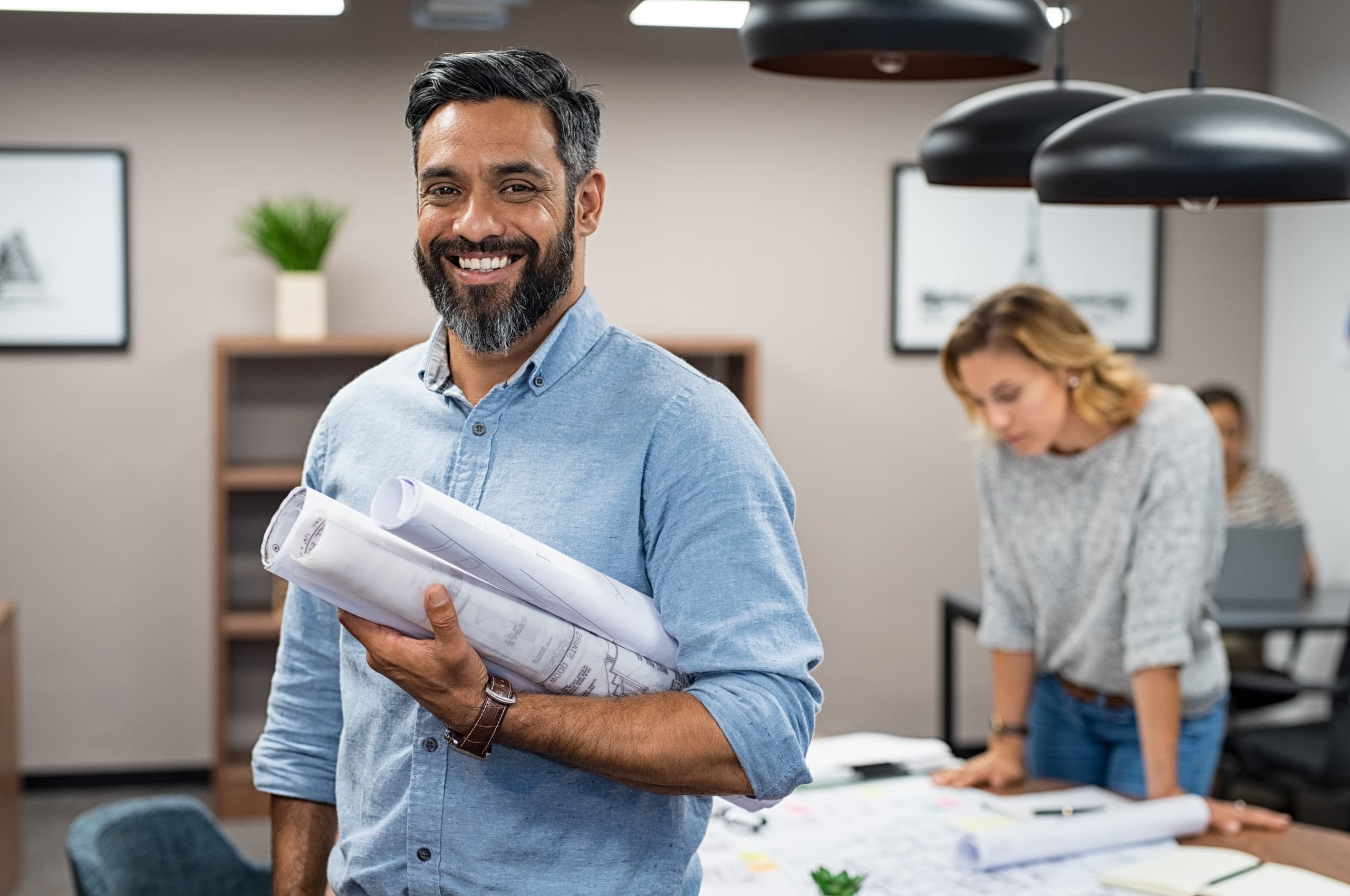 An architect smiles at the viewer while colleagues work on in the background